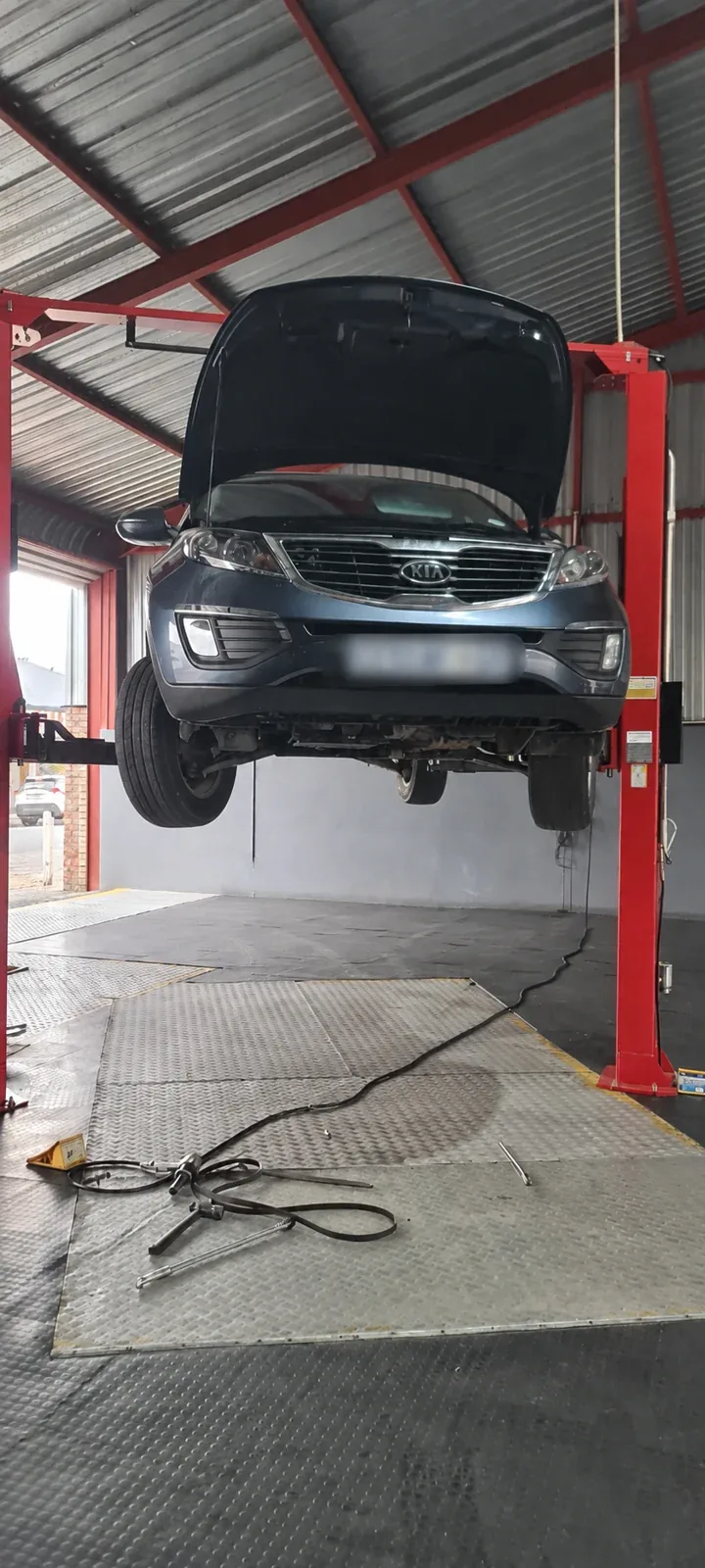 A vehicle on a workshop lift for repairs, with its number plate blurred.